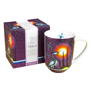 May include: A ceramic mug and its matching box featuring a purple background with a stylised crane, a bright sun, and dark pine trees. The box displays the text "ARTISTS", "CRANE LA GRUE", and "J. JACKO". The mug has a white interior and a handle.