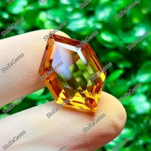 May include: A faceted, hexagonal-shaped orange gemstone with a transparent, polished surface. The gem displays internal light reflections and sharp geometric edges, showcasing a vibrant, warm amber hue throughout its crystalline structure.