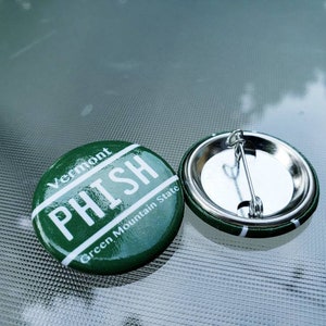 May include: Green and white button with the text "Vermont PHISH Green Mountain State" on it. The back of the button has a silver pin.