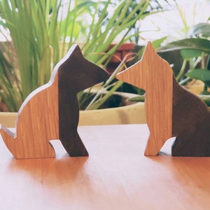 May include: Two wooden dog figurines, one brown and one light brown, sitting side by side on a wooden surface.