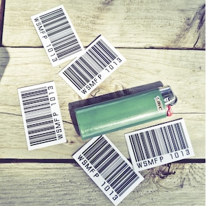 May include: Four white barcode stickers with the text "WSMF P 1013" on a wooden surface. A green lighter with the text "BIC" is on top of the stickers.