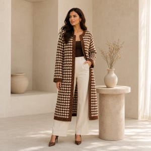 May include: A long, open-front cardigan featuring a brown and cream houndstooth pattern, worn over a dark brown top and cream-colored wide-leg trousers. The cardigan has long sleeves and a straight hemline that falls below the knees.