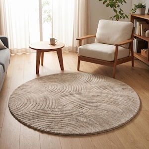 May include: A round, beige area rug featuring a textured, raised pattern of concentric semicircles. The rug has a soft, plush appearance with varying shades of light brown and tan, creating a subtle, repeating wave-like design across its surface.