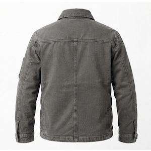May include: A charcoal gray jacket featuring a structured collar, long sleeves with buttoned cuffs, and a vertical seam running down the center of the back. The garment is constructed with visible topstitching and a horizontal yoke across the shoulders.
