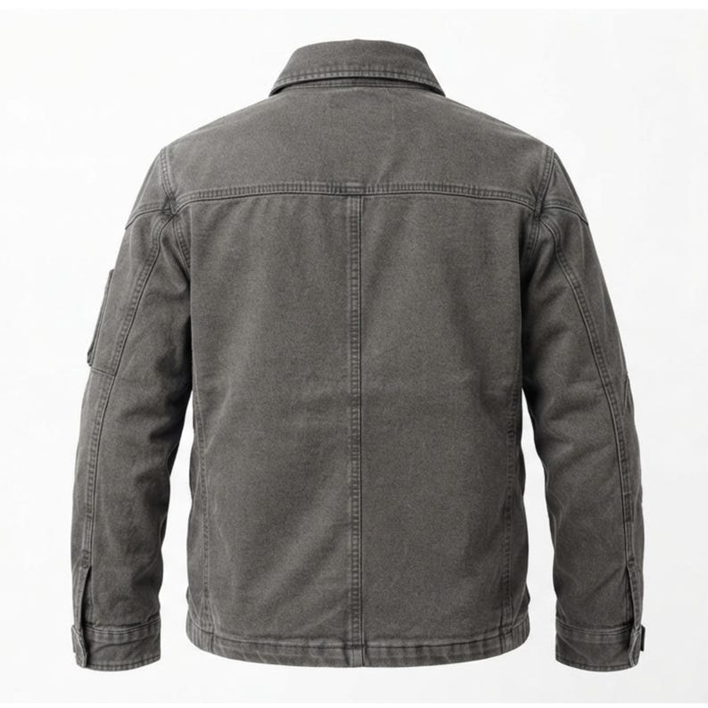 May include: A charcoal gray jacket featuring a structured collar, long sleeves with buttoned cuffs, and a vertical seam running down the center of the back. The garment is constructed with visible topstitching and a horizontal yoke across the shoulders.