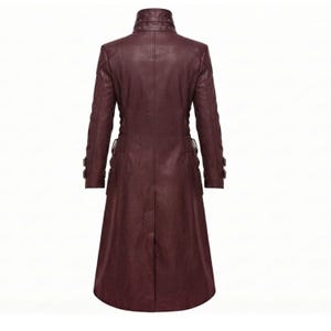 May include: A long, dark burgundy coat made of a smooth material, featuring a high collar with buckle detailing, long sleeves with buckled cuffs, and a structured, tailored fit that extends to the mid-calf with a central back vent.