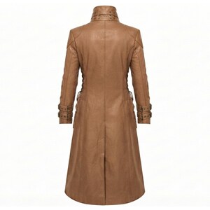 May include: A tan long-length coat featuring a high collar with decorative studs, long sleeves with buckled straps at the cuffs, and a central back vent. The garment is constructed with structured seams and a smooth finish throughout the design.