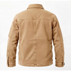 May include: A tan-colored jacket featuring a classic collar, long sleeves with buttoned cuffs, and a structured back panel with vertical stitching. The garment is constructed with durable fabric, showcasing reinforced seams and a clean, uniform finish.