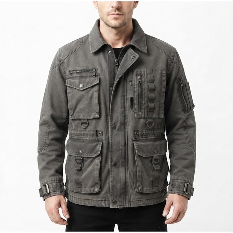 May include: A charcoal gray utility jacket featuring a fold-down collar, a front zipper closure with a snap-button placket, multiple chest and waist pockets with flaps, vertical zippered compartments, D-ring attachments, and adjustable sleeve cuffs.