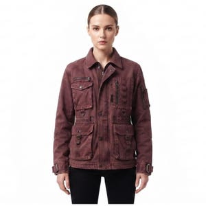 May include: A dark maroon utility jacket featuring a collared neckline, a front button closure, and multiple pockets. The jacket includes two chest pockets, two lower pockets, a zippered sleeve pocket, and metal D-ring hardware accents.