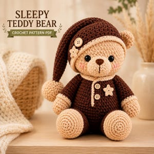 Puede incluir: Un oso de peluche tejido a ganchillo que lleva un gorro de dormir marrón oscuro con un pompón y un mameluco marrón oscuro a juego con detalles en beige claro. El oso tiene dos botones pequeños en el pecho, una aplicación en forma de estrella y el texto SLEEPY TEDDY BEAR.
