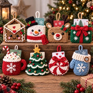 May include: A collection of eight crocheted Christmas ornaments designed as gift card holders. The set includes a gingerbread envelope, a snowman, a reindeer, a green gift box, a cocoa mug, a Christmas tree, a peppermint candy, and a blue mitten.