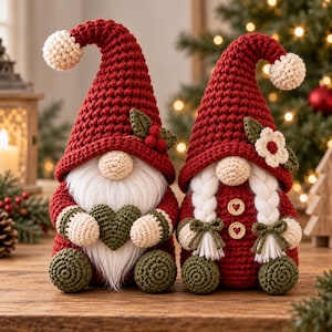 May include: Two crocheted gnomes with red pointed hats topped with cream pom-poms. The left gnome has a white beard and holds a green heart. The right gnome features white braided hair, two wooden heart buttons, and a small white flower on the hat.