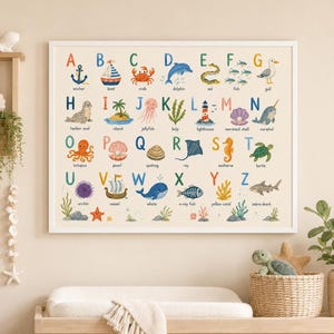 May include: A white-framed wall poster featuring an ocean-themed alphabet chart. Each letter from A to Z is paired with a colorful watercolor illustration of a sea creature or nautical object, including an anchor, boat, crab, dolphin, and whale.