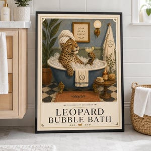 May include: A framed wall art print titled LEOPARD BUBBLE BATH from The Good Life Collection. It depicts a leopard with a white towel wrapped around its head, relaxing in a blue clawfoot bathtub filled with bubbles, holding a cocktail glass.