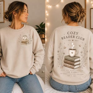 Könnte beinhalten: Ein beigefarbenes Sweatshirt mit Rundhalsausschnitt und einer kleinen Grafik auf der linken Brust, die eine dampfende Tasse auf Büchern zeigt. Der Rücken zeigt eine große Illustration einer Tasse auf einem Bücherstapel mit dem Text COZY READER CLUB.