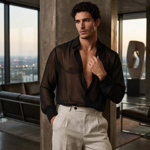 May include: A long-sleeved black shirt made of a sheer, translucent fabric with a classic collar and button-down front, paired with high-waisted off-white trousers featuring a single visible button closure and a pleated front design.