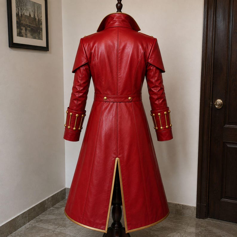 May include: A long red coat featuring a high collar, shoulder capes, and a waist belt with gold-toned buttons. The cuffs are adorned with vertical gold-toned bars and studs. The coat has a central back vent with gold trim along the bottom hem.