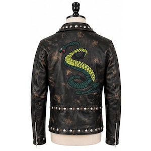 May include: A black leather jacket with a distressed finish, featuring a large embroidered snake in shades of green and yellow on the back. The jacket includes silver-toned metal studs along the collar and hem, and silver zippers on the cuffs.