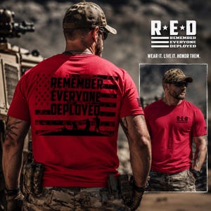 May include: A red short-sleeved t-shirt featuring a black graphic of the American flag with the text REMEMBER EVERYONE DEPLOYED. The back displays the full flag design with silhouettes of soldiers, while the front chest shows the R.E.D. logo.