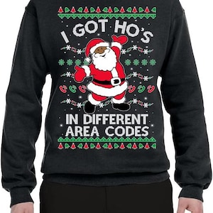 May include: A dark charcoal gray long-sleeve sweatshirt featuring a graphic of Santa Claus in the center. The text reads I GOT HO'S IN DIFFERENT AREA CODES. The design includes red and green telephone icons, snowflakes, and Christmas trees.