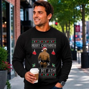 May include: A black long-sleeve sweatshirt featuring a graphic print of a person wearing a Santa hat and boxing gloves, with the text MERRY CHRITHMITH IN MY ATH! surrounded by a festive pattern of snowflakes, holly, and red boxing gloves.