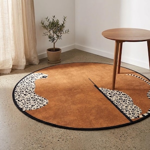 May include: A round area rug featuring a brown background with a stylised leopard print pattern along the edges. The rug has a black border and depicts the head and tail of a leopard in a minimalist graphic style, creating a circular design.