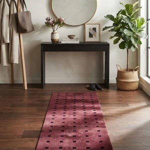 Puede incluir: Una alfombra de pasillo rectangular en un tono rojo burdeos profundo, con un patrón repetitivo de pequeños acentos cuadrados de color negro oscuro dispuestos en líneas verticales sobre la superficie, colocada sobre un suelo de madera oscura.