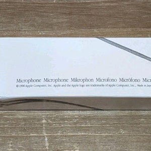 May include: A white rectangular product box for an Apple microphone. The box features the word Microphone in a serif font, a graphic of a microphone, and text listing the word in multiple languages with 1990 Apple Company copyright information.