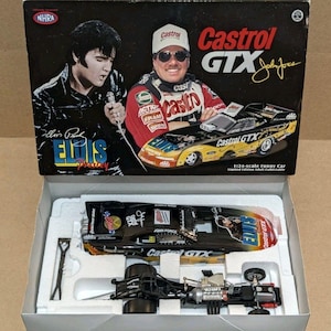 May include: A 1:24-scale Castrol GTX Funny Car model in a box featuring Elvis Presley and John Force. The set includes a black and yellow race car body with Elvis graphics, a detailed chassis with engine components, and a small black tool.