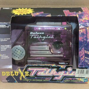 Pode incluir: Um gravador de cassetes Deluxe Talkgirl roxo translúcido com função de alteração de voz, em embalagem preta original com detalhes gráficos coloridos, apresentando um microfone retrátil embutido e operação fácil com apenas uma mão.