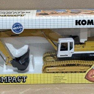 Może przedstawiać: Żółto-czarny model koparki z odlewu metalowego Komatsu PC400LC w prostokątnym kartonowym pudełku. Opakowanie posiada wzór w kratkę, logo Komatsu oraz ilustrację osoby w ogrodniczkach pokazującej kciuk w górę.
