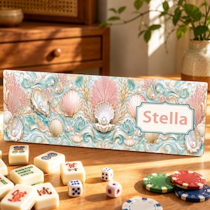 Può includere: Un supporto rettangolare per tessere del mahjong con un design costiero caratterizzato da corallo rosa, conchiglie bianche, perle e motivi a onde blu. Il nome Stella è stampato in lettere rosa all'interno di una cornice decorativa.