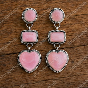 May include: A pair of drop earrings featuring three stacked pink stone segments in silver settings. Each earring consists of a round top, a rectangular middle, and a heart-shaped bottom piece, all framed with a twisted rope-style silver border.