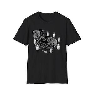 May include: A black short-sleeve t-shirt featuring a white graphic print of a Smith chart surrounded by six lit candles and an electronic test instrument connected by a cable. The design is centered on the chest of the garment.