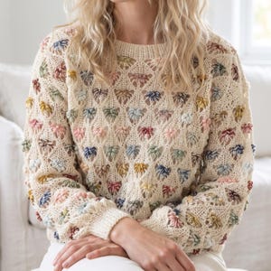 May include: A cream-colored long-sleeve knit sweater featuring an openwork diamond pattern. The garment is decorated with small, raised, multi-colored yarn clusters in shades of pink, blue, yellow, and green distributed throughout the knit.