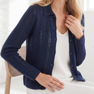 Op de afbeelding: Een marineblauw vest met lange mouwen, een kraag, een knoopsluiting aan de voorzijde en verticale breipatronen met verfijnde opengewerkte details op de mouwen en het lijfje, gedragen over een eenvoudig wit mouwloos hemd.