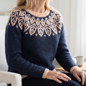 May include: A long-sleeved knit sweater featuring a dark navy blue base color with a contrasting light peach-colored yoke. The yoke displays a repeating leaf-like pattern in the same peach tone, complemented by matching peach ribbed cuffs and neckline.