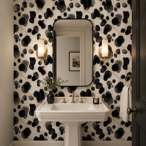 May include: A bathroom vanity area featuring a white pedestal sink with brass taps, a rectangular mirror with a black frame, and two wall-mounted cylindrical sconces. The wall is covered in wallpaper with a black and grey watercolour dot pattern.