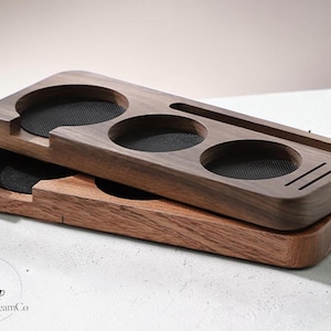 Puede incluir: Dos organizadores rectangulares de madera apilados uno sobre otro. Cada organizador presenta tres aberturas circulares con inserciones negras texturizadas, una ranura larga y estrecha, y tres pequeñas ranuras paralelas en la superficie superior.