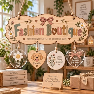Könnte beinhalten: Ein hängendes Holzschild mit der Aufschrift Fashion Boutique und Personalized Gifts for Brighter Days, das vier hängende Ornamente zeigt: ein Gänseblümchen, eine Hundeillustration mit dem Namen Charlie, ein Blumenmotiv und ein Herz mit Small Business Big Heart.