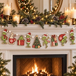May include: A decorative garland featuring wooden cutouts of a green character in a Santa hat, a red mug with a candy cane, a decorated Christmas tree, and stacked gift boxes, all strung together with white beads on a natural twine cord.