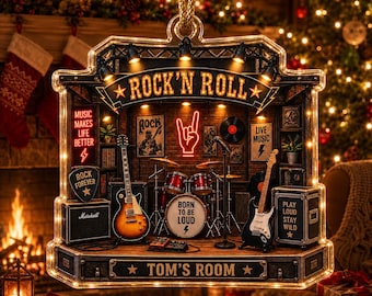 May include: A decorative hanging ornament shaped like a rock music stage, featuring a sunburst electric guitar, a drum kit with a bass drum labeled BORN TO BE LOUD, a black electric guitar, amplifiers, and neon-style signs reading ROCK'N ROLL and TOM'S ROOM.