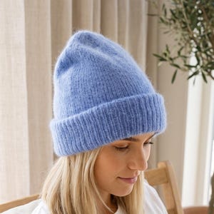 Könnte beinhalten: Eine hellblaue Strickmütze mit umgeschlagenem Bündchen. Die Mütze hat eine weiche, flauschige Textur und ein durchgehendes Rippstrickmuster. Sie ist mit einer abgerundeten Krone gefertigt und sitzt eng am Kopf für vollständige Abdeckung.