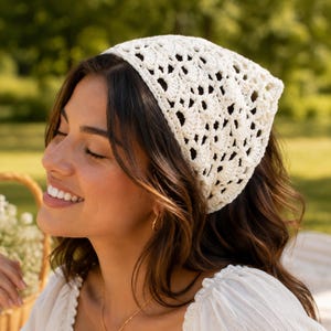 Könnte beinhalten: Ein dreieckiges Kopftuch aus cremeweißem Garn in einem komplizierten, durchbrochenen Häkelmuster. Das Accessoire weist ein sich wiederholendes geometrisches Design mit kleinen rautenförmigen Aussparungen im gesamten Stoff auf, was eine leichte Textur erzeugt.