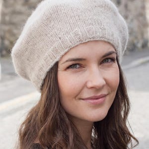 Könnte beinhalten: Eine hellbeige Strickbére mit einer strukturierten, flauschigen Oberfläche und einem gerippten Rand. Die Mütze hat eine klassische, abgerundete Form und bietet eine warme, bequeme Passform, die den oberen Teil des Kopfes mit einem schlichten Design bedeckt.