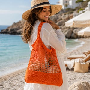 Könnte beinhalten: Eine leuchtend orangefarbene Häkel-Tragetasche mit einem offenen Netzdesign im oberen Bereich und einem festen, engmaschig gehäkelten Boden. Die Tasche verfügt über zwei integrierte Schulterriemen und besteht aus einem kräftig gefärbten Garnmaterial.