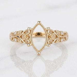 May include: A gold ring featuring a central marquise-shaped setting frame. The band is decorated with sculpted rose motifs and leaves, accented with small clear stones embedded along the sides of the shank, creating a detailed metal structure.