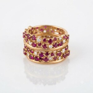 May include: A stack of two gold rings featuring a cluster design of round-cut red rubies and small clear white diamonds. The bands have a smooth, polished finish, and the gemstones are set in a dense, organic arrangement across the top surface.