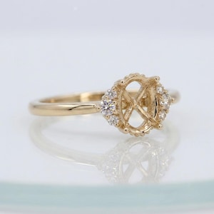 Peut inclure: Une bague en or dotée d'un sertissage circulaire central conçu pour accueillir une pierre précieuse. Le sertissage est flanqué de chaque côté par un groupe de trois petites pierres rondes, claires et étincelantes, créant un aspect raffiné.